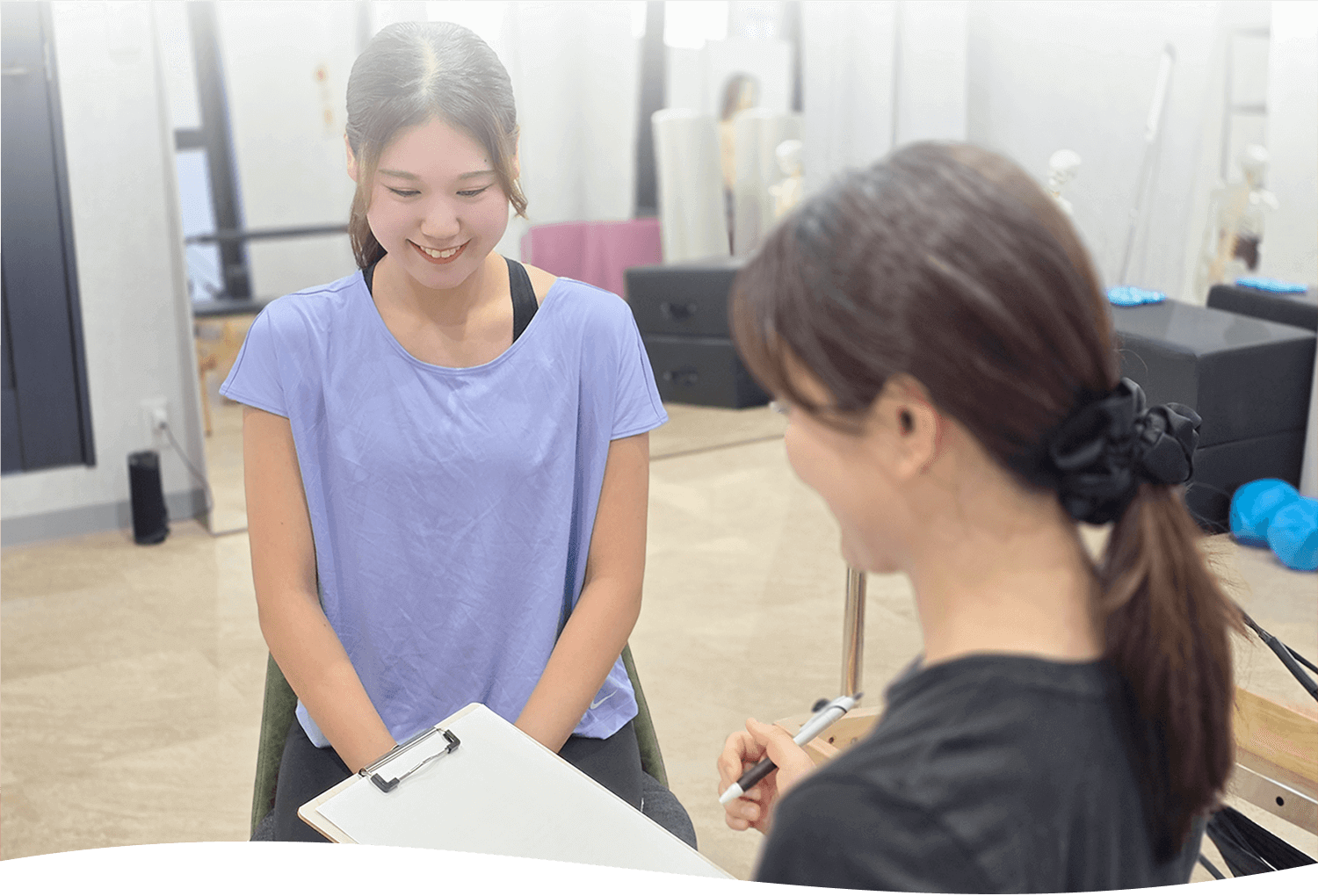 女性のインストラクターの方がファイルを持っていて一人の女性に話を聞いている画像