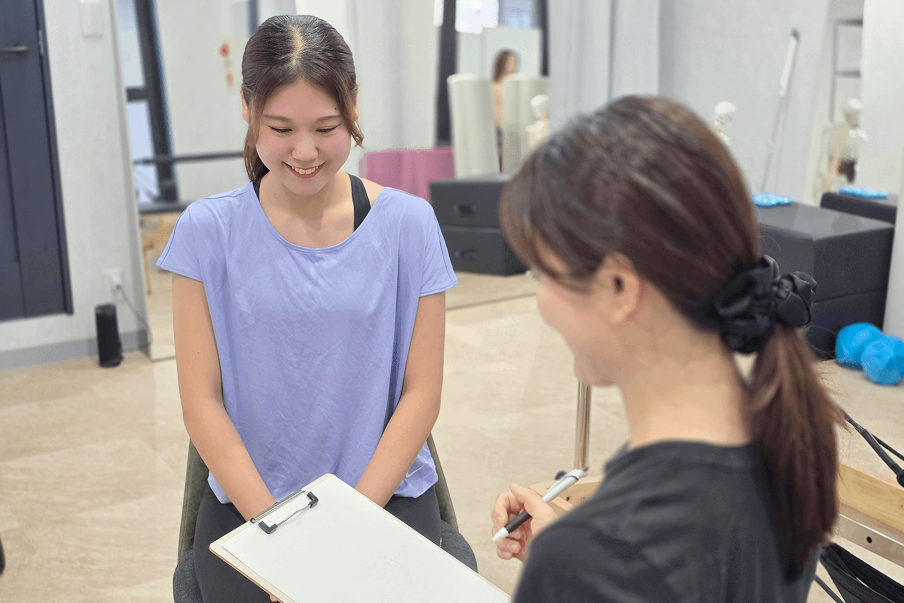 女性のインストラクターの方がファイルを持っていて一人の女性に話を聞いている画像