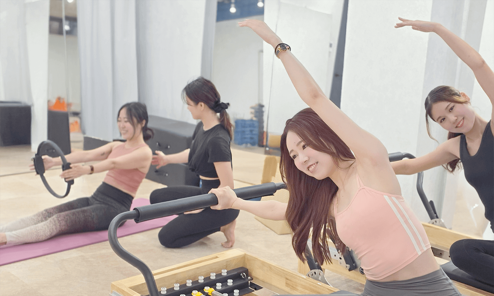 右に女性二人が片手をあげてストレッチをしていて左には女性のインストラクターが一人の女性に指導している画像